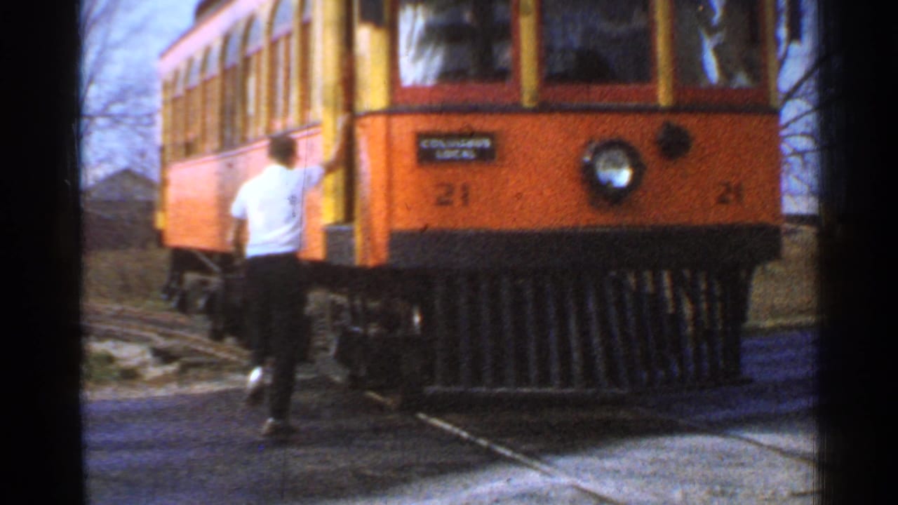 A man boards an orange and yellow trolley marked 21 in Connecticut, with tracks visible below.