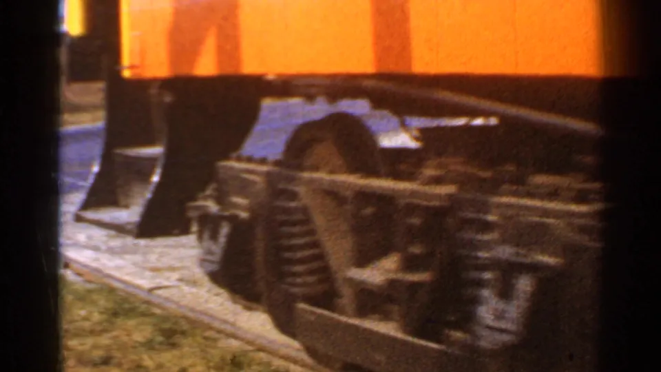 1953 Connecticut 8mm close-up of a rail car truck and wheel assembly beneath an orange body on yard track.