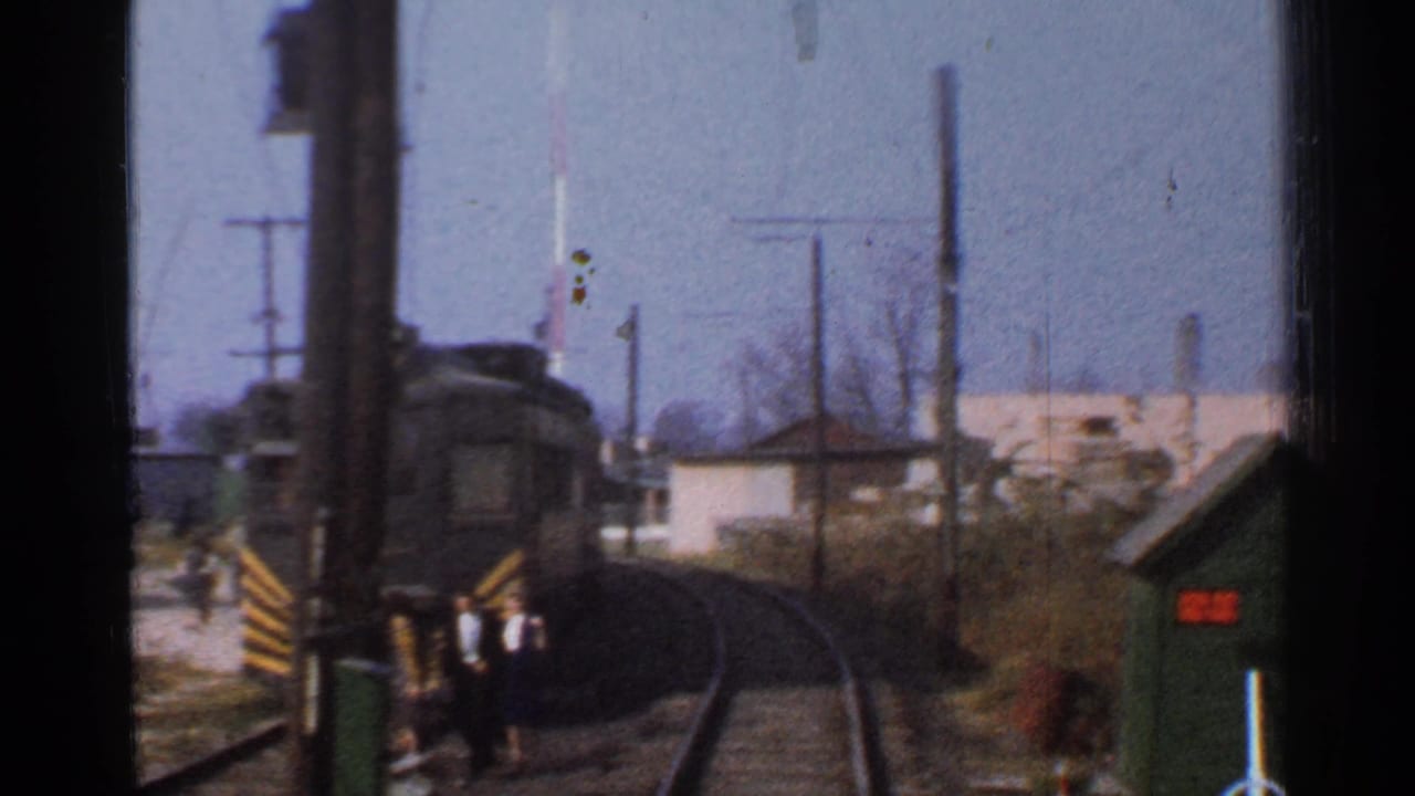 Front-of-train view on curved tracks with bystanders near a crossing gate.