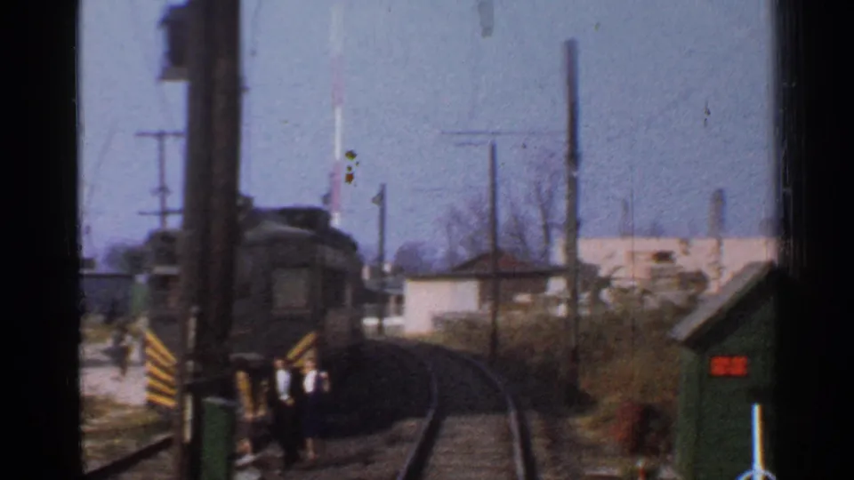 1953 Connecticut train POV approaching curved tracks, with people beside a striped crossing gate and utility poles.