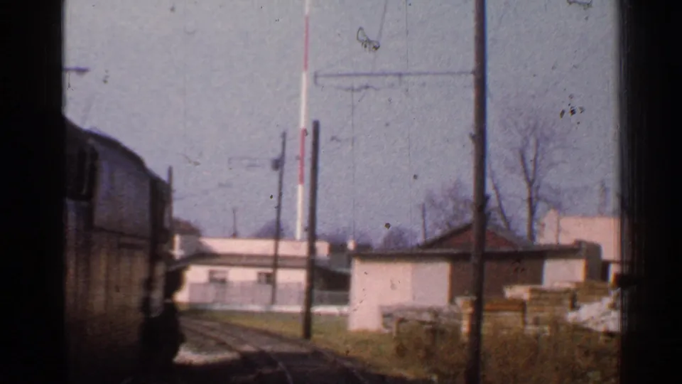 Passenger-window view in Connecticut, 1953, showing curving rails, a passing train car, low structures, poles, bare trees, and trackside materials.