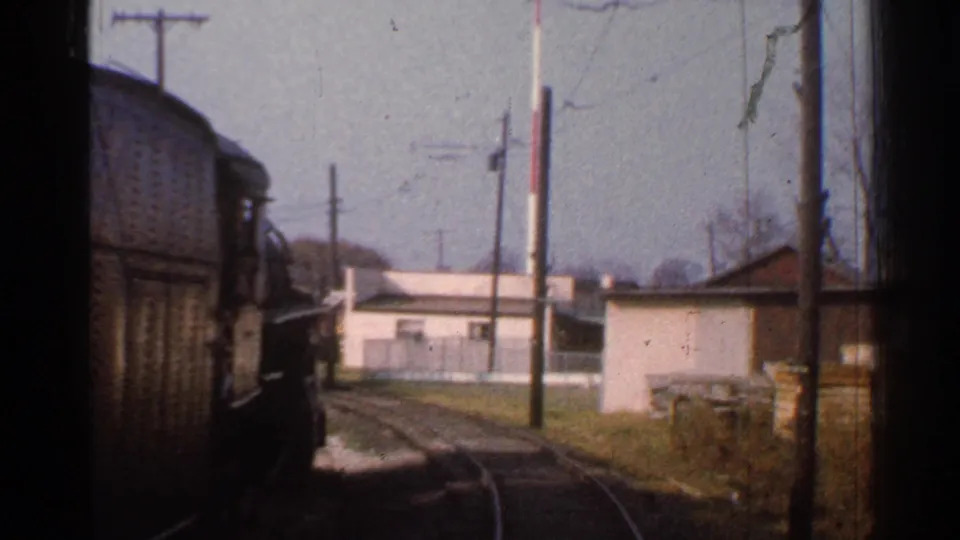 1953 Connecticut train-window frame with a rail car beside curved track, low lineside buildings, utility poles, grass, and bare trees.