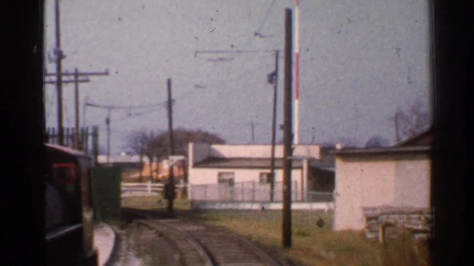 1953 Connecticut passenger-view rail shot showing a train edge, curving tracks, signal post, utility poles, small buildings, and fencing.