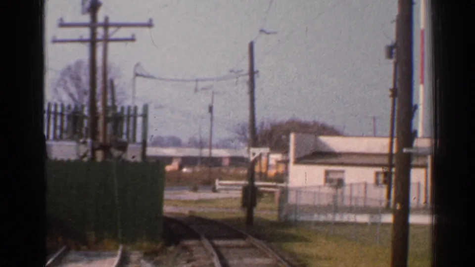 1953 Connecticut rail view from a moving train, with curving tracks, green fencing, utility poles, small buildings, grass, and pale sky.