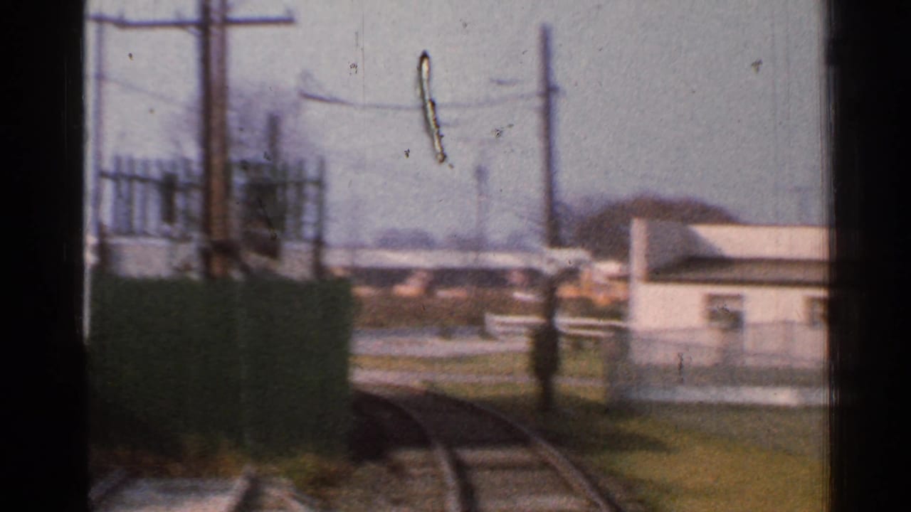 1953 Connecticut train POV showing curving rails, a green fence, utility poles, and small trackside buildings.