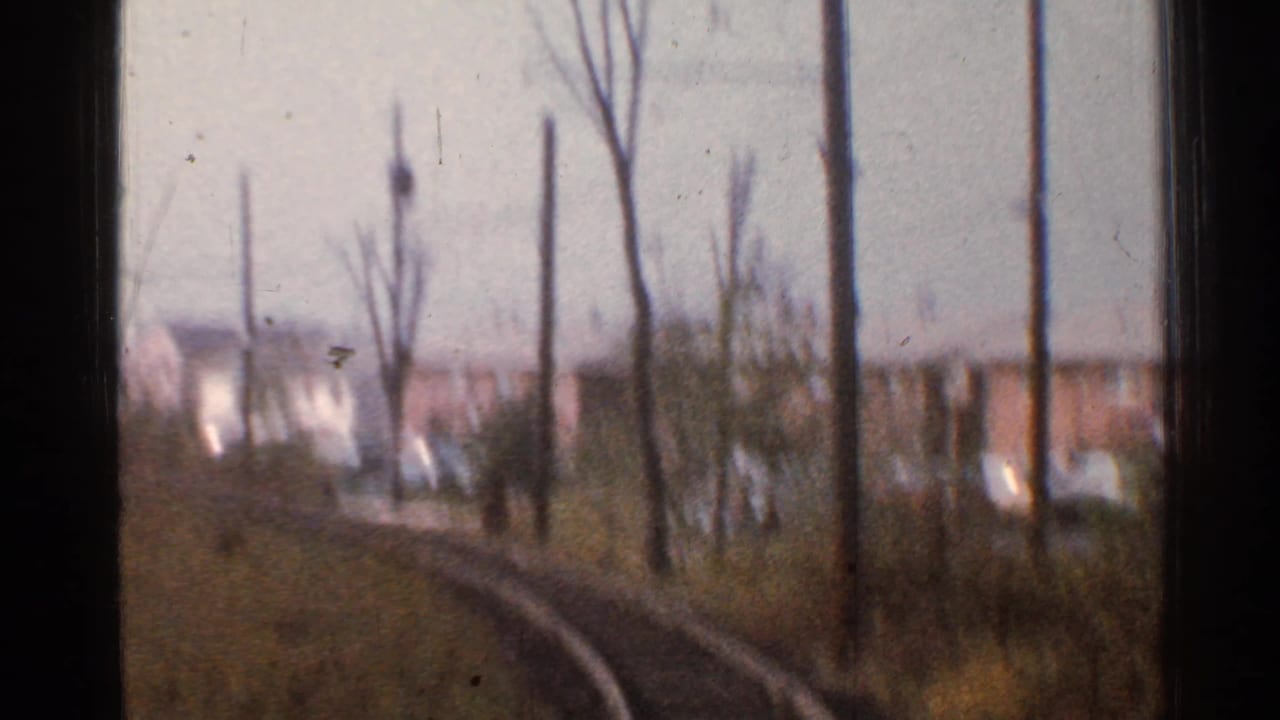 1953 Connecticut 8mm frame from a moving train, showing curving tracks past bare trees, utility poles, grass, and distant houses.