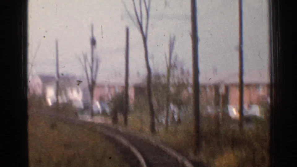 1953 Connecticut 8mm frame from a moving train, showing curving tracks past bare trees, utility poles, grass, and distant houses.