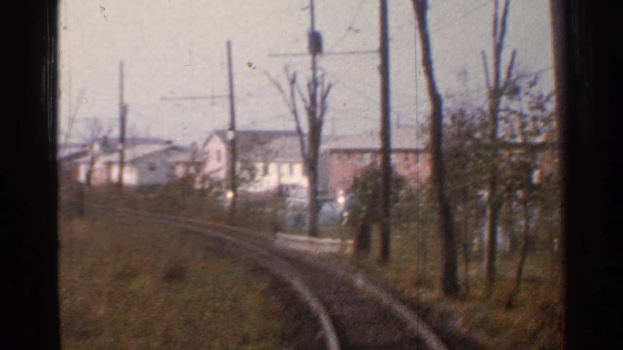 Rail line bends past utility poles and small houses, partly framed by the train window.
