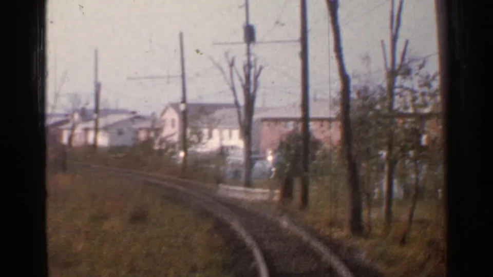 Moving 8mm view in Connecticut, 1953, with rails curving beside utility poles, bare trees, and modest white and brick houses.