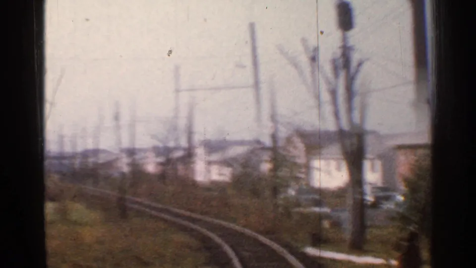 Soft, motion-blurred 1953 Connecticut rail view with trackside poles, bare trees, low houses, grass, and the train window edge.