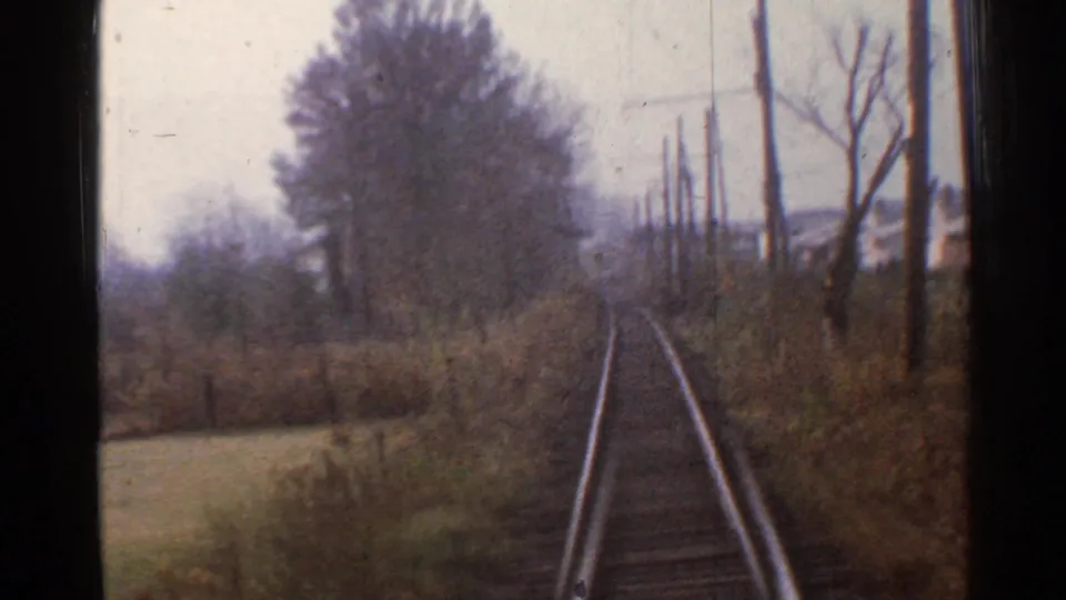 1953 Connecticut 8mm train POV showing tracks ahead, leafless trees, brush, and utility poles along a rural rail line.