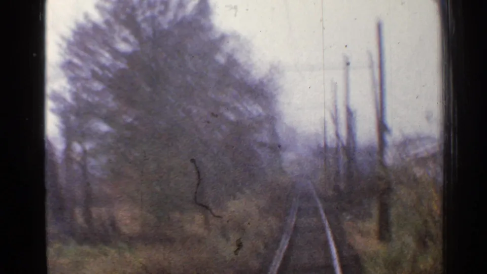 Soft 8mm Connecticut train POV with motion blur over tracks, winterlike trees, brush, and poles beside the rail line.