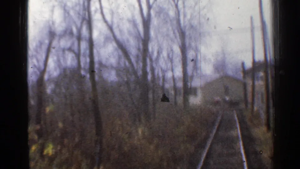 A moving 8mm train view in Connecticut shows tracks, bare trees, poles, and a small pale trackside building in 1953.