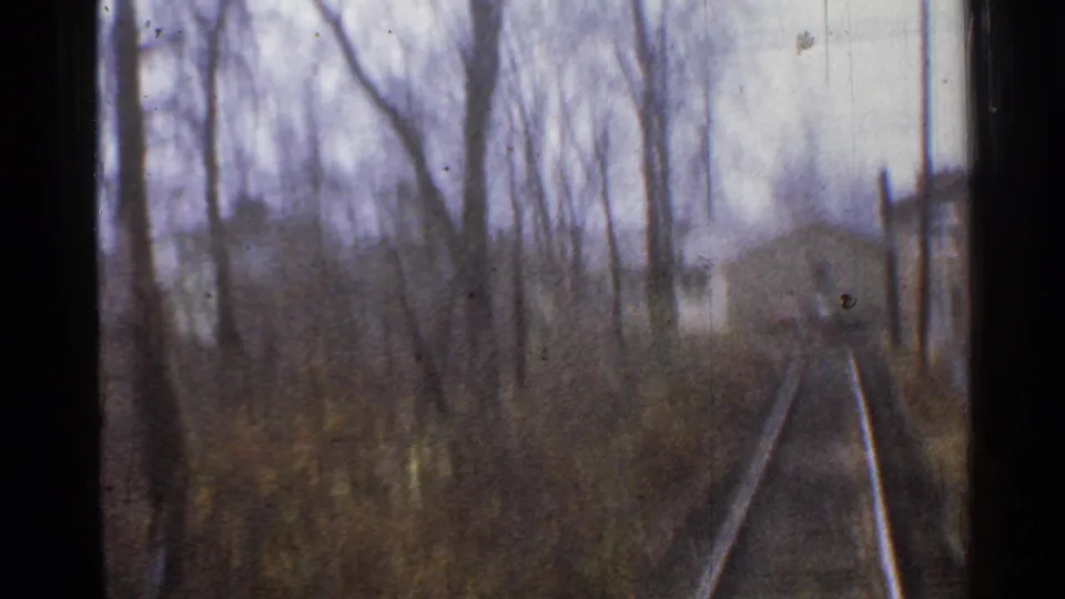 1953 Connecticut 8mm frame looking down railroad tracks from a moving train, with bare trees, brush, and soft focus.