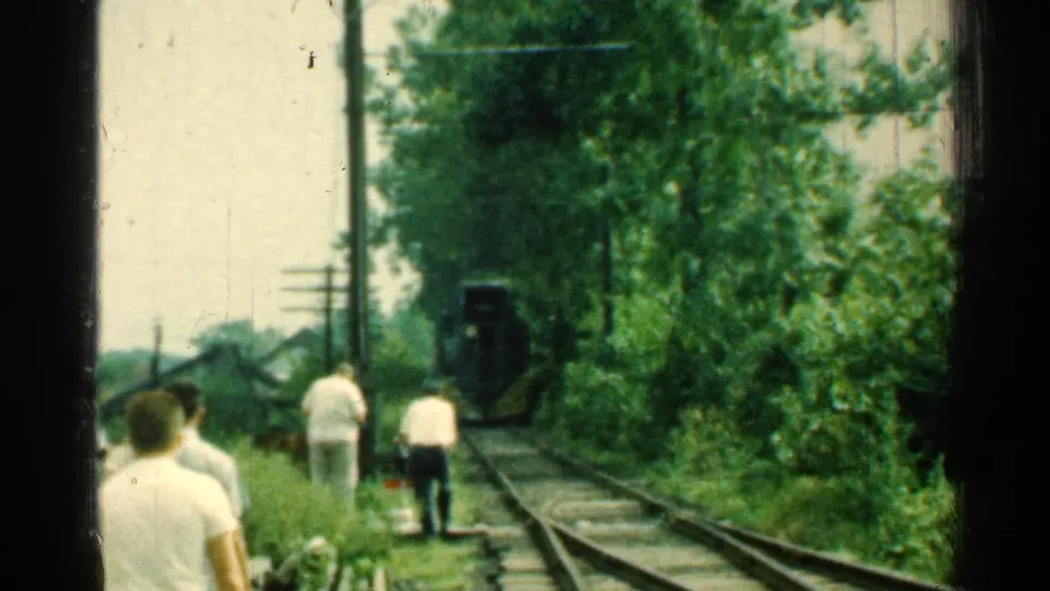 1953 Connecticut rail scene with men in white shirts near the tracks and a dark rail vehicle ahead with yellow detail.