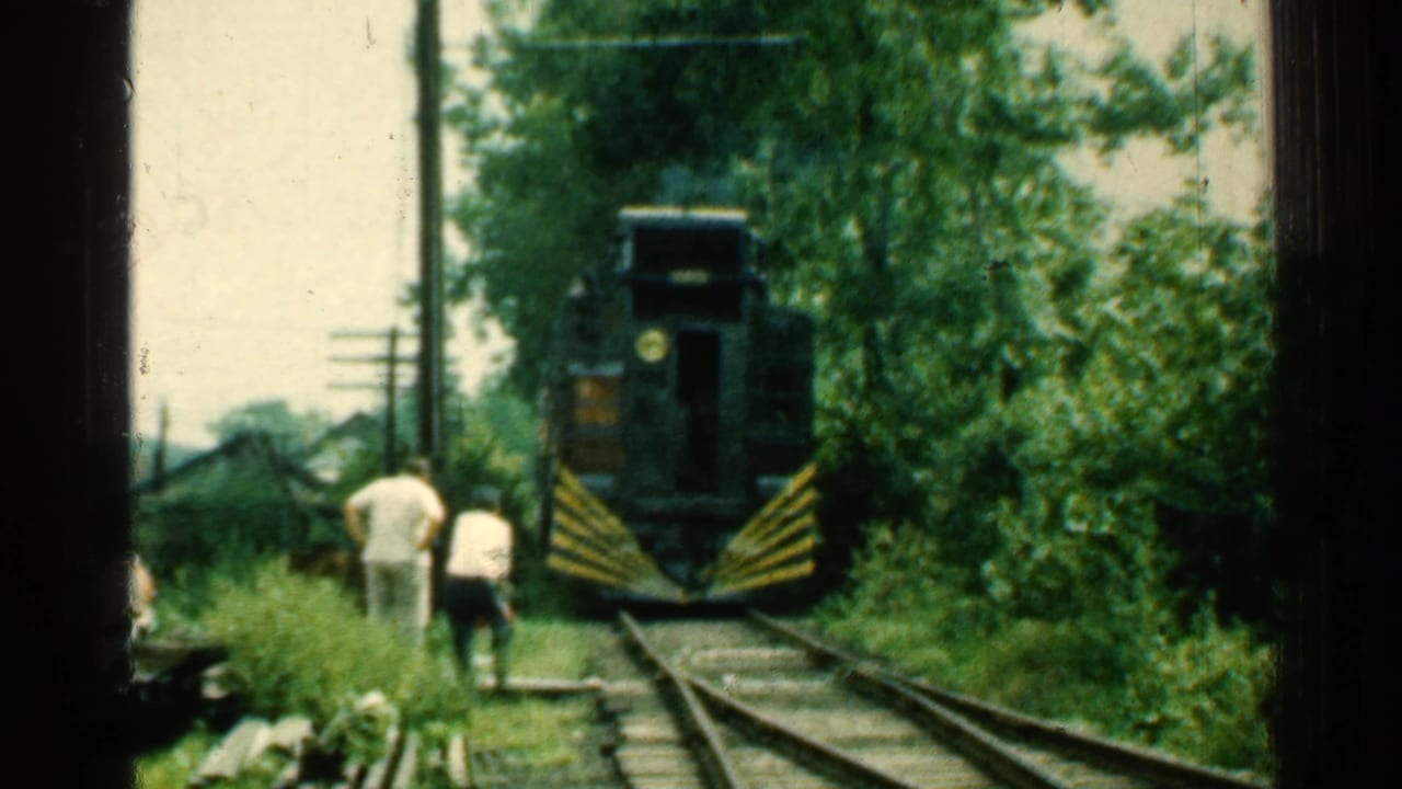 Train approaching two men standing beside rural railroad tracks.