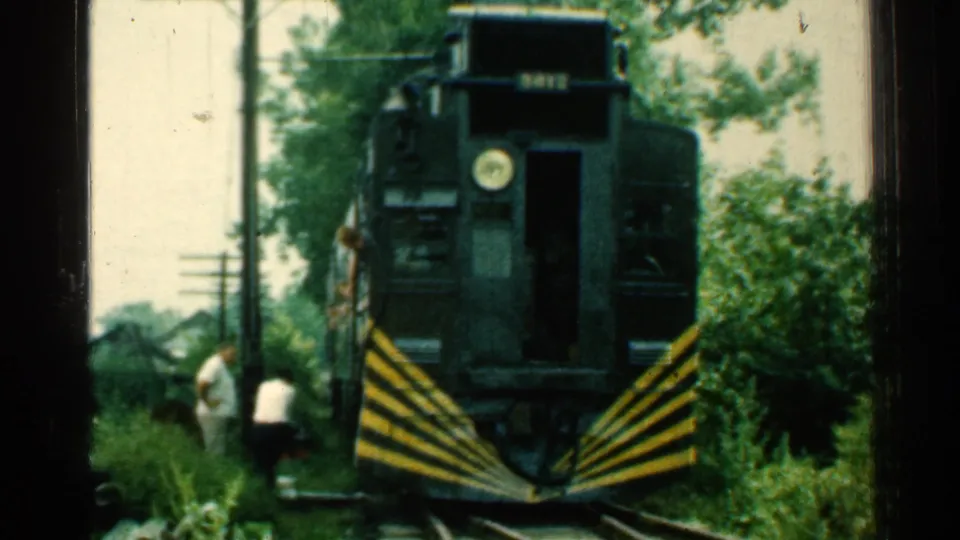 Close 1953 Connecticut frame of the train front, striped pilot, open doorway, and two men standing beside the tracks.