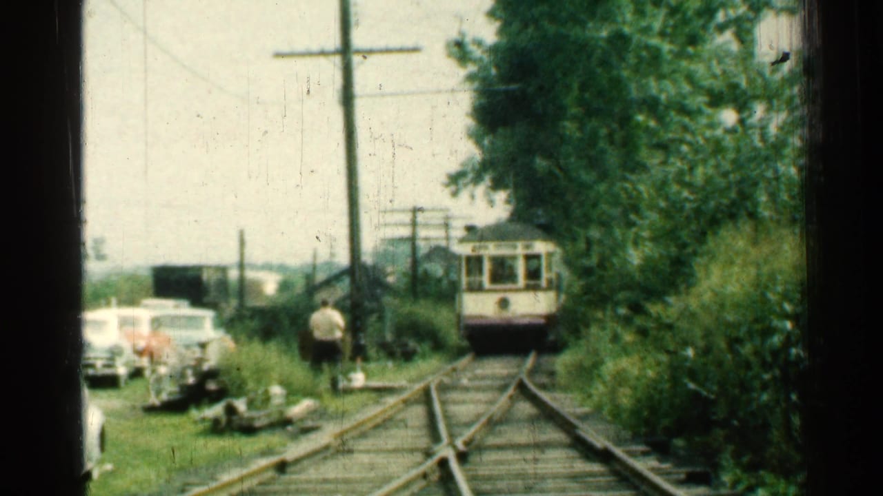 1953 Connecticut 8mm frame showing a distant trolley on wooded tracks with cars and a person near the left side.