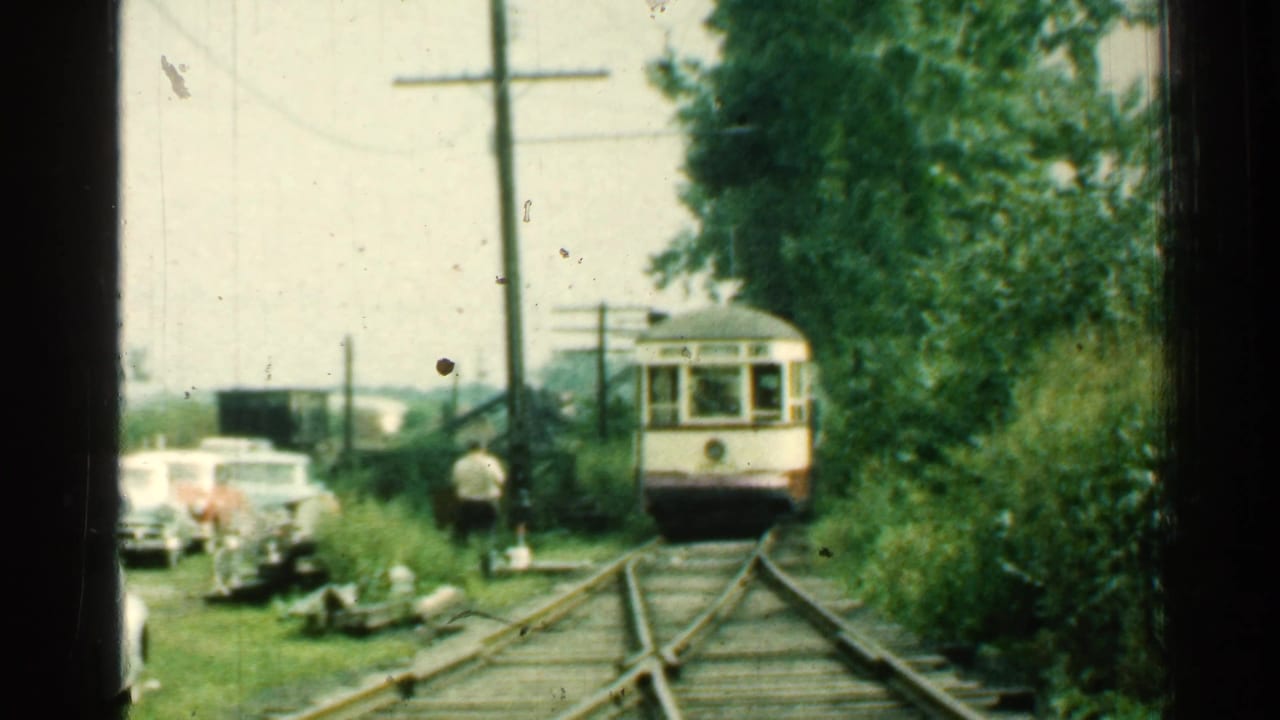1953 Connecticut trolley footage with the streetcar closer on the tracks, framed by trees, utility poles, cars, and a standing man.