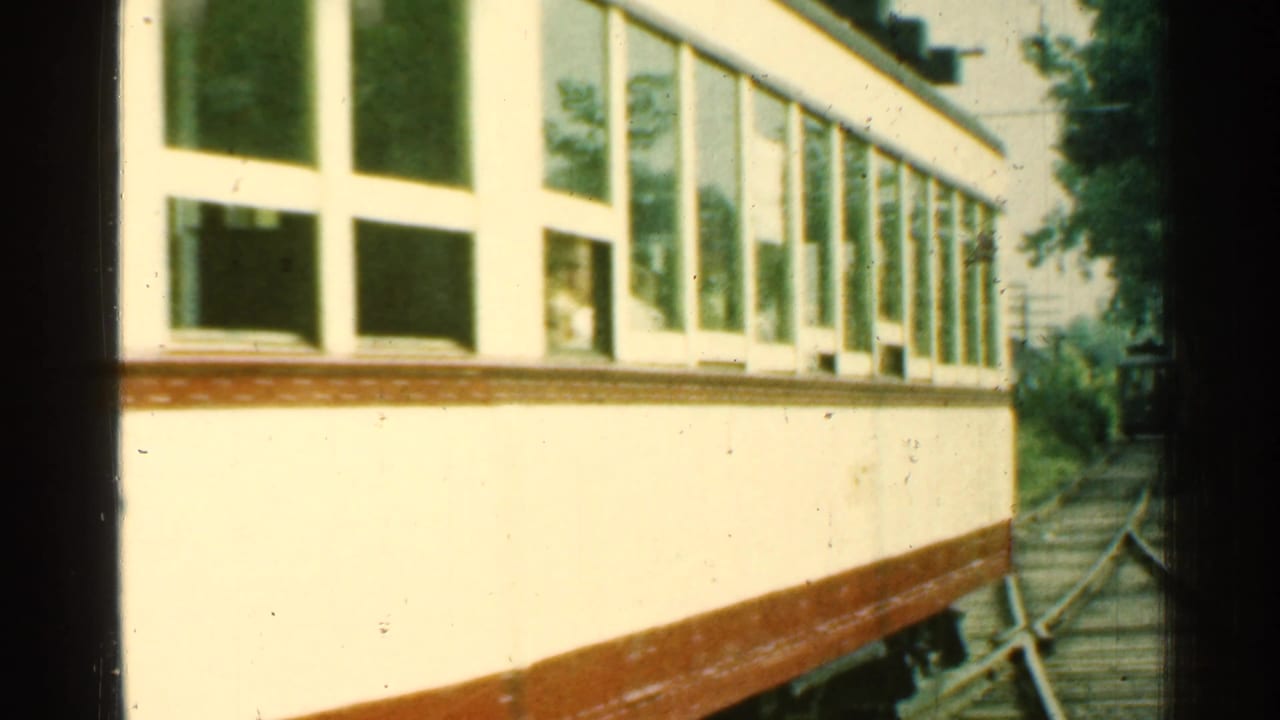 Close side view of the 1953 Connecticut trolley moving past, with large windows, brown lower trim, and trackside trees.