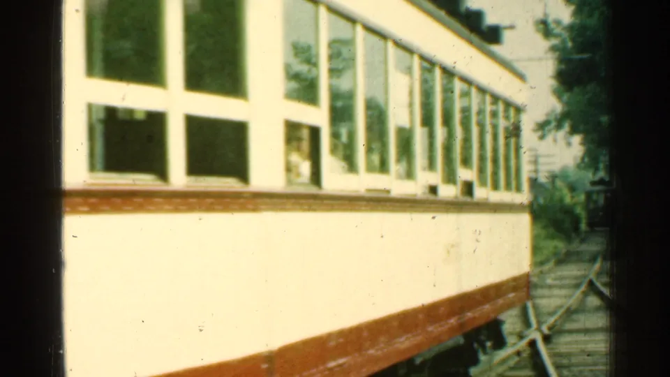 Close side view of the 1953 Connecticut trolley moving past, with large windows, brown lower trim, and trackside trees.