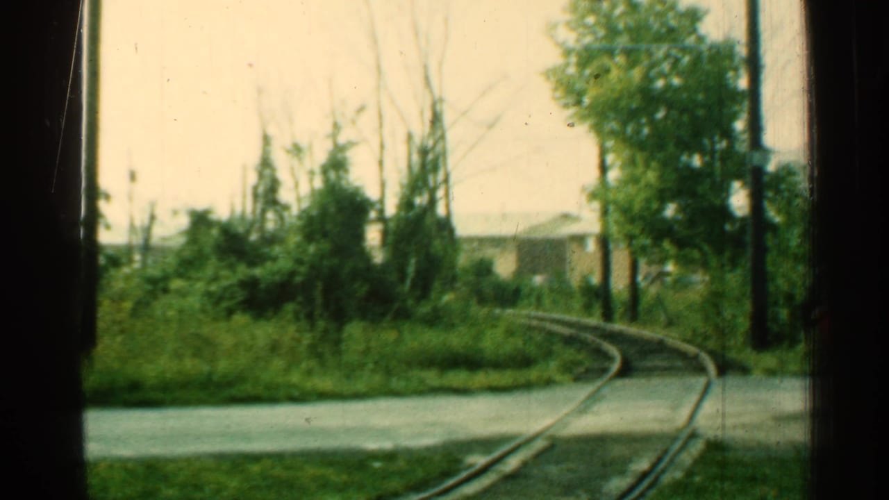 Curved rail track runs past trees and brush, viewed through dark vertical window framing.