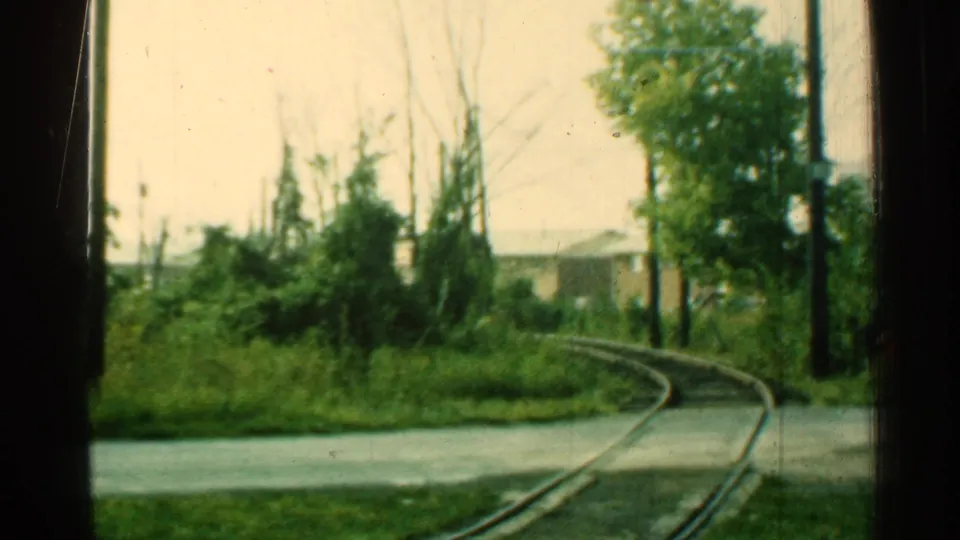 1953 Connecticut 8mm frame showing a curved trolley track, paved crossing, trees, brush, and dark window-frame edges.