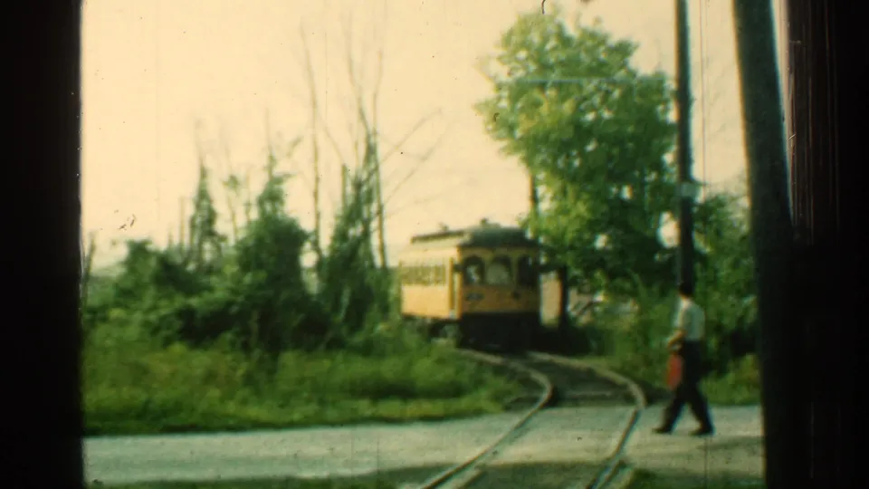 Adult man crosses the track area in front of an approaching yellow trolley in 1953 Connecticut home-movie footage.