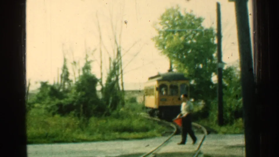 1953 Connecticut frame with an adult man stepping across the curved trolley track as the yellow car nears the crossing.