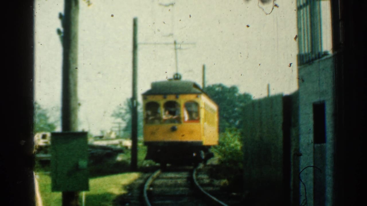 Yellow trolley approaching on curved tracks beside a utility box and poles.