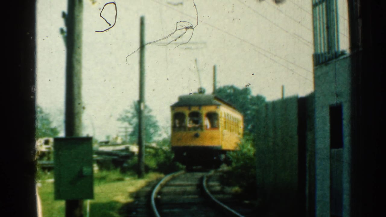 The yellow trolley continues around the bend in Connecticut, framed by trackside poles, grass and a building edge.