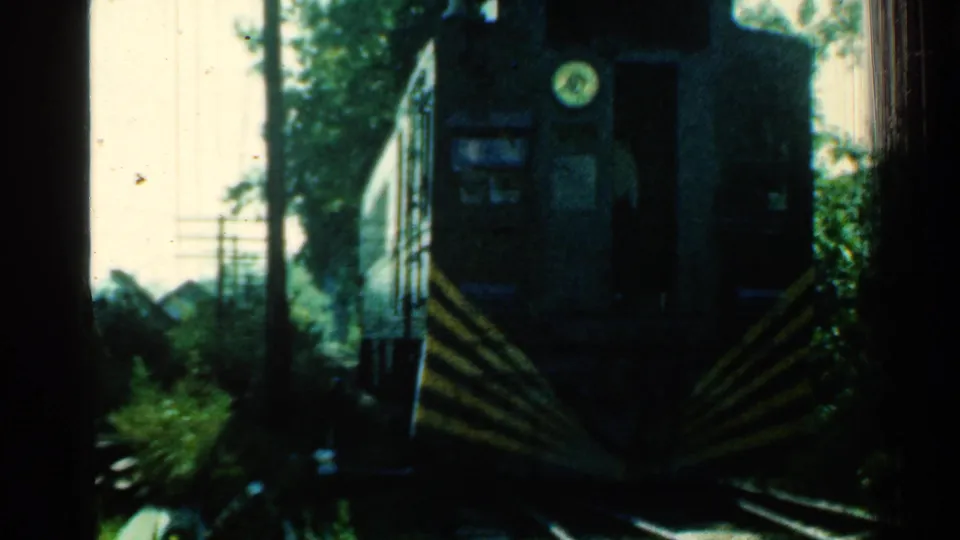 1953 Connecticut home-movie frame with a close front view of a dark train moving along wooded tracks.