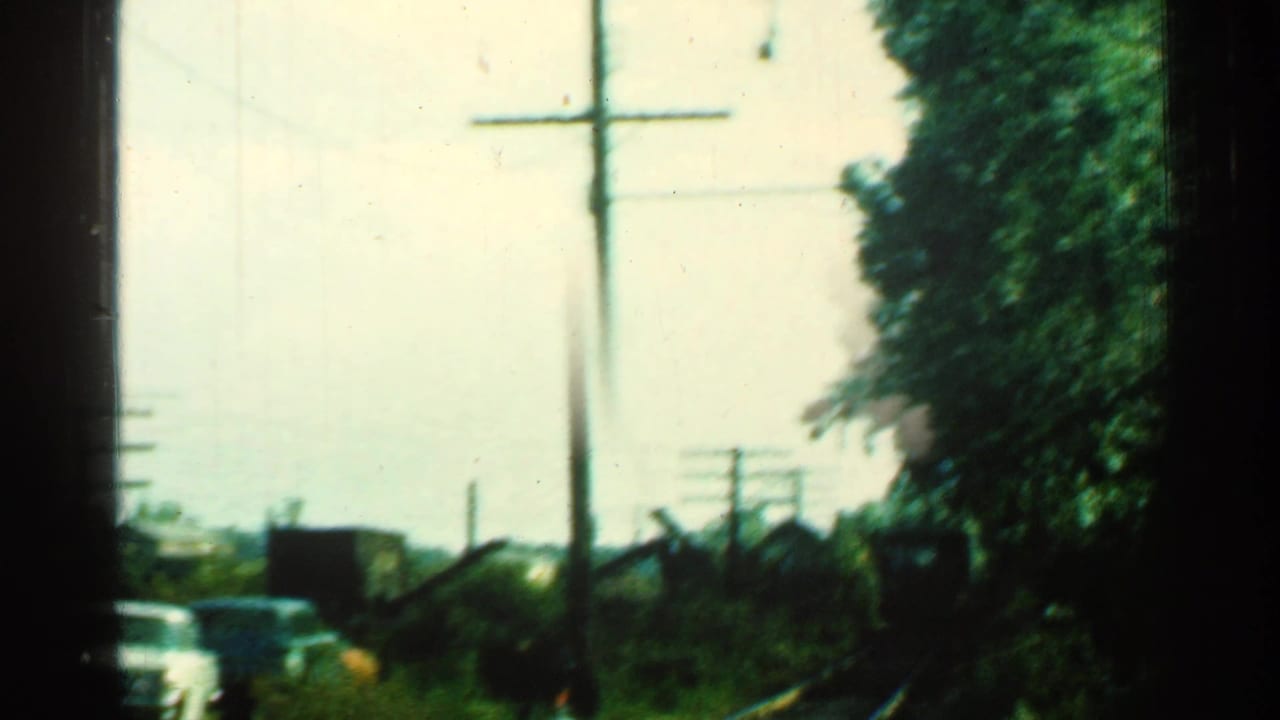 Rail tracks beside a road with cars, utility poles and trees in soft 8mm color.