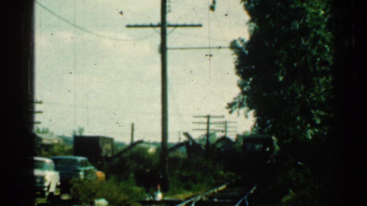 1953 Connecticut 8mm frame with a red train or rail vehicle entering at right beside tracks, cars, trees and utility poles.