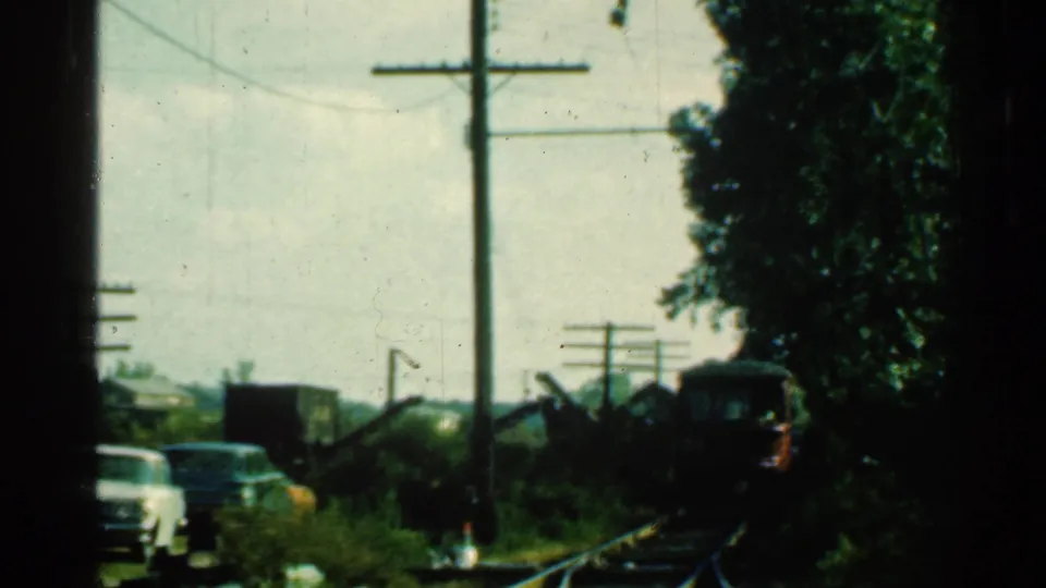 1953 Connecticut home-movie view of a red train approaching on tracks near roadside cars, trees and utility poles.