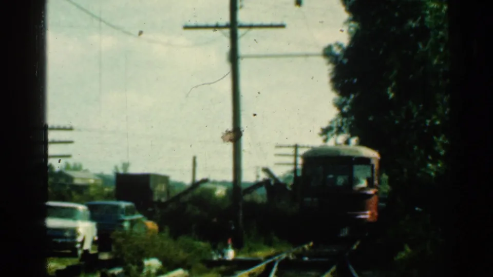 1953 Connecticut frame showing the red train close to the camera at right, with rail tracks, cars, poles and trees around it.