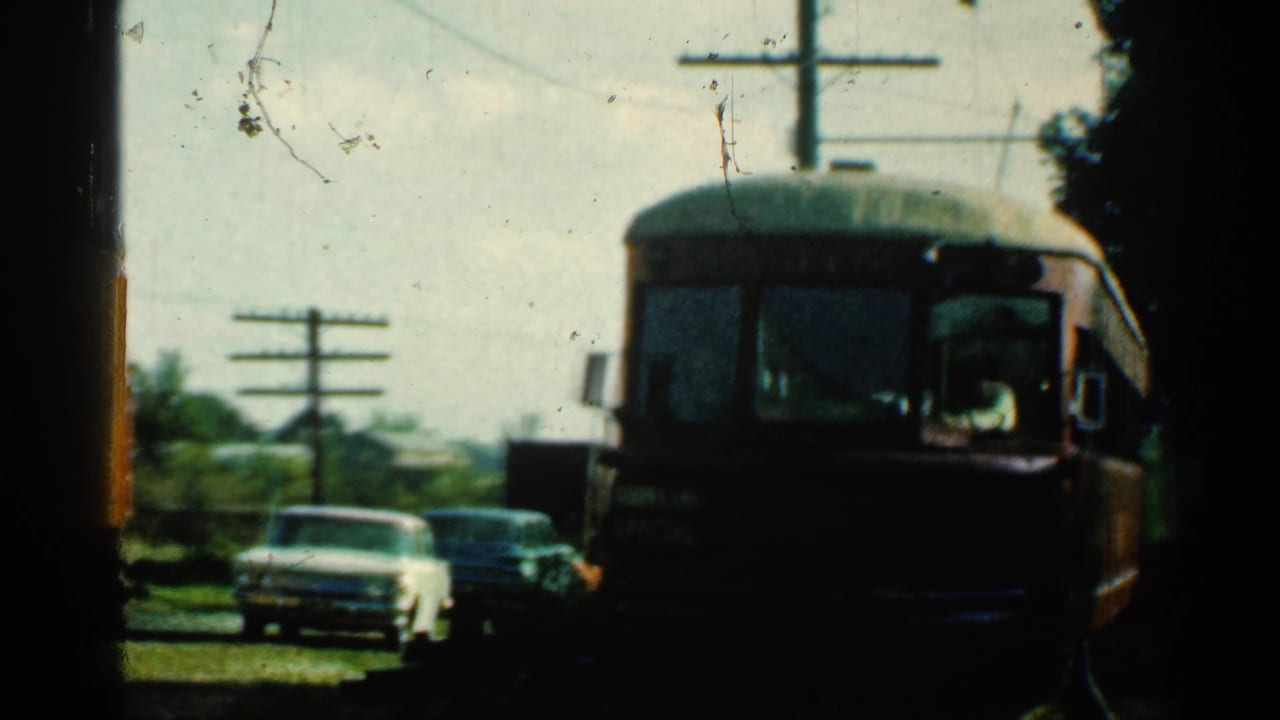Red train closer to camera with cars and utility poles behind it.