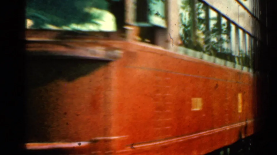 The red train passes close to the lens, filling most of the 8mm frame with its side panels and windows.