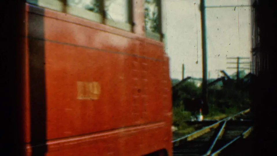 The red train continues past the camera, revealing rails, utility poles, and trackside greenery in the Connecticut setting.