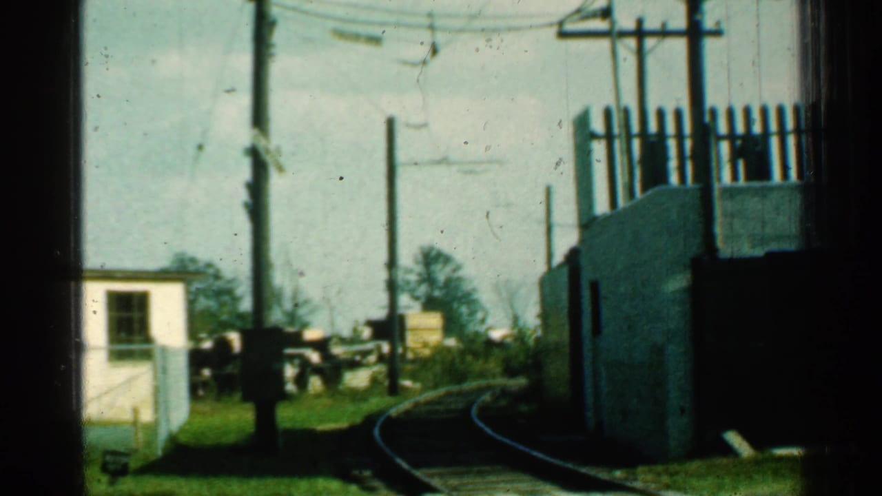 1953 Connecticut 8mm frame showing curved trolley tracks, utility poles, overhead wires, and a small white trackside building before the trolley enters view.