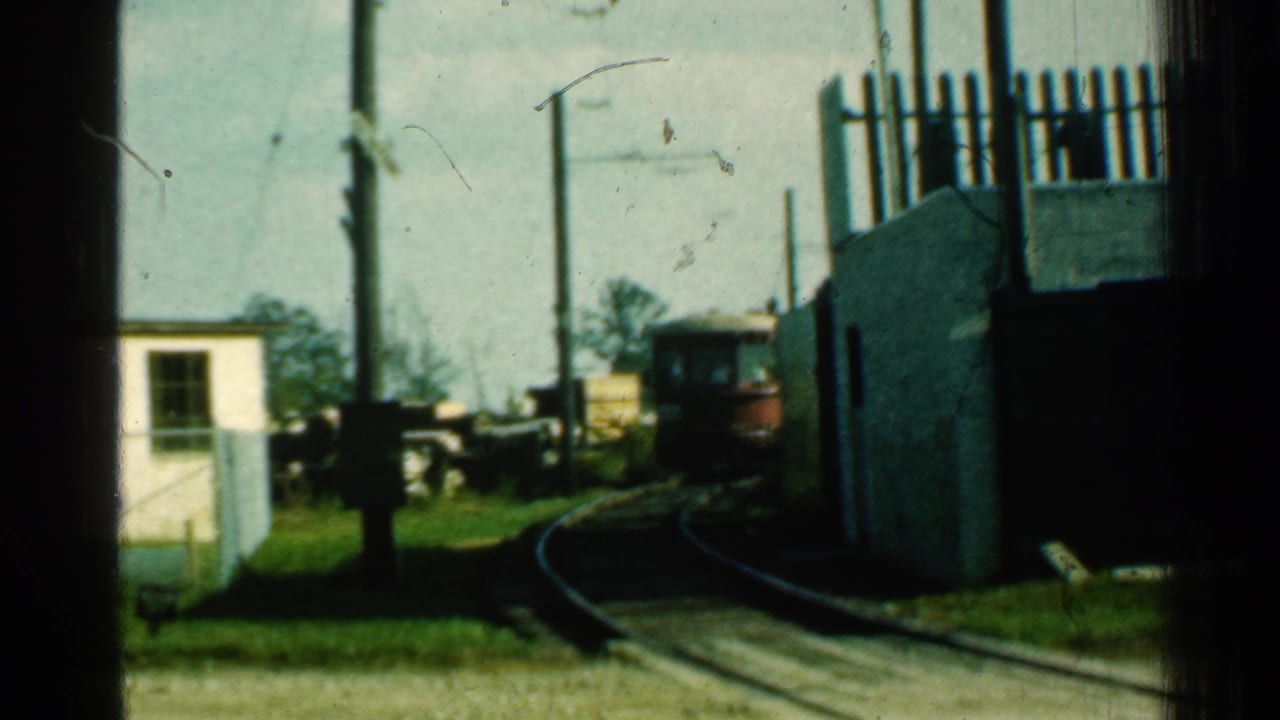 A red trolley appears in the distance on curved narrow tracks, with overhead power lines, poles, grass, and trackside structures visible in Connecticut footage from 1953.