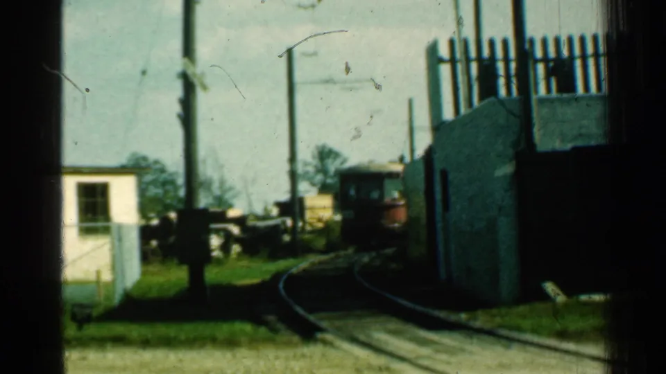 A red trolley appears in the distance on curved narrow tracks, with overhead power lines, poles, grass, and trackside structures visible in Connecticut footage from 1953.