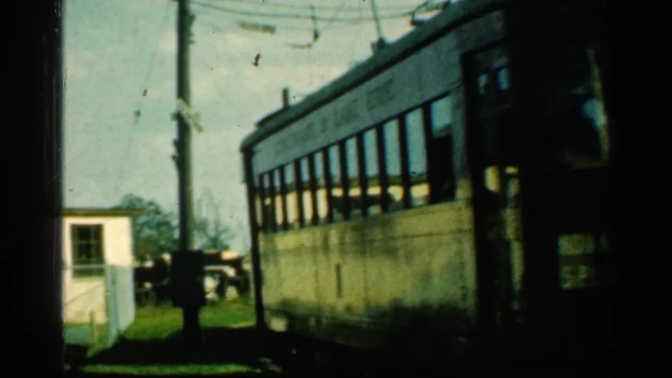 Side view of the Connecticut trolley passing through the frame, showing long window rows, cream bodywork, trackside grass, and nearby poles.