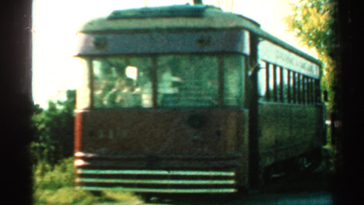 1953 Connecticut 8mm frame showing a brown trolley car near the camera on rails, with trees, brush, and overhead wire nearby.