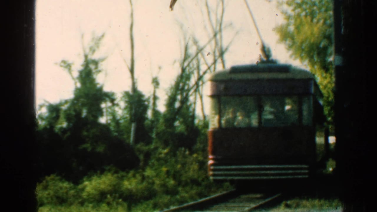 1953 Connecticut 8mm frame with the brown trolley receding on curved rail tracks through trees, brush, and overhead trolley wires.