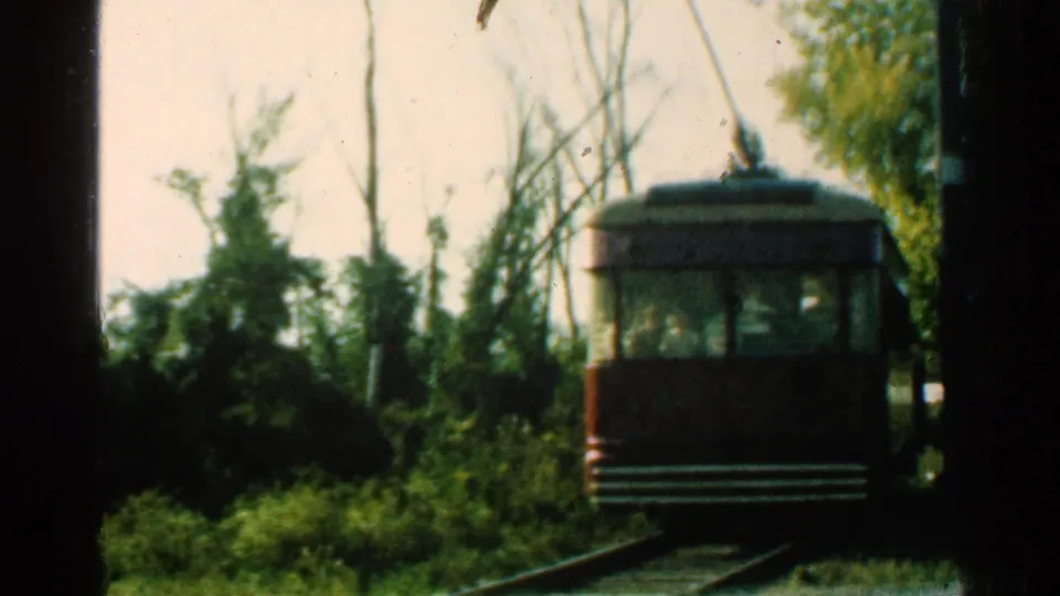1953 Connecticut 8mm frame with the brown trolley receding on curved rail tracks through trees, brush, and overhead trolley wires.