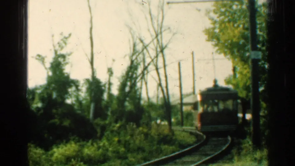 1953 Connecticut 8mm frame with the trolley small in the distance on a curving track, surrounded by trees, brush, and overhead wires.