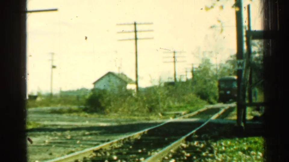 1953 Connecticut frame showing trolley rails curving beside roadside vegetation, utility poles, and a small light-colored building.