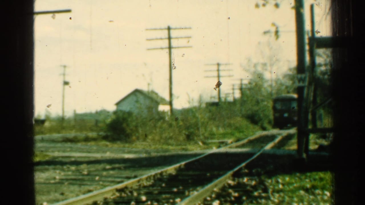 1953 Connecticut 8mm frame showing rural tracks, utility poles, brush, a small white house, and a train approaching in the distance.