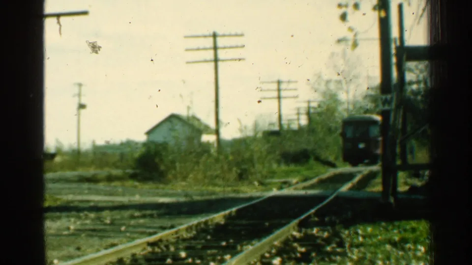 Final frame shows the train close to the rural Connecticut crossing, with parallel rails, utility poles, brush, and a small white house behind.